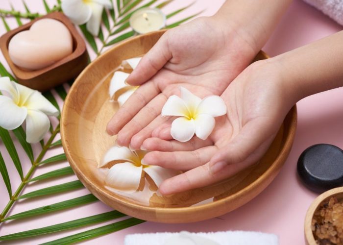woman-soaking-her-hands-in-bowl-of-water-and-flowers-spa-treatment-and-product-for-female-feet-and-hand-spa-massage-pebble-perfumed-flowers-water-and-candles-relaxation-flat-lay-top-view
